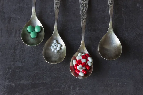 Bir sürü bir kaşık karanlık bir arka plan üzerinde renkli hapları ve ilaçlar, vitaminler, kapsül. Kavram-eczane, gıda katkı maddeleri, kötüye kullanımı ve bağımlılığı ilaç ilaçlar, uyuşturucu bağımlılığı.