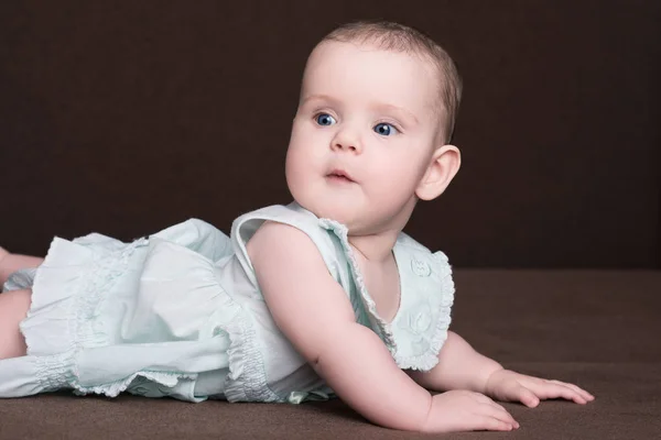 Yazlık elbise karnı üzerinde koyu kahverengi zemin üzerinde büyük mavi gözleri yalan ile sürpriz küçük bebeğim