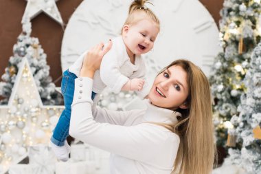 Şirin bebek kızı ile Noel ve yeni yıl tatilleri üzerinde oynarken mutlu genç anne. Çocuk ile anne Noel ağacı ve bulanık şenlikli ışıkları ile dekore edilmiş Oda