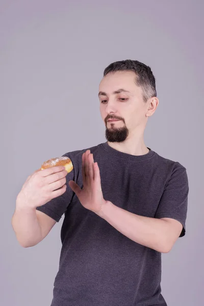 Mann mit Bart isst Brötchen vor grauem Hintergrund — Stockfoto