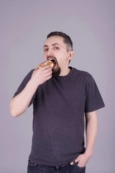 Man med ett skägg som äter en bulle över grå bakgrund — Stockfoto