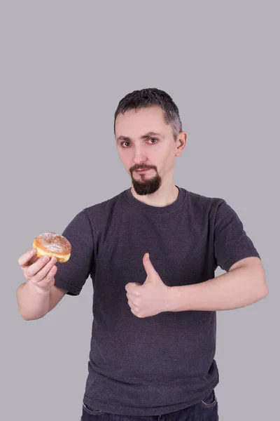 Mann mit Bart isst Brötchen vor grauem Hintergrund — Stockfoto