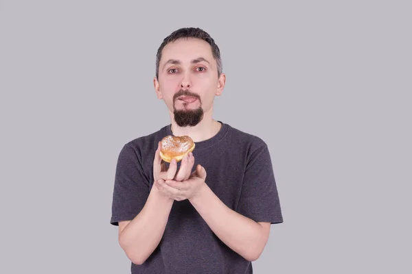 Man met een baard eten van een broodje over grijze achtergrond — Stockfoto