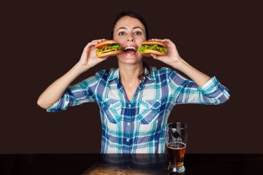 Kahverengi arka planda izole bira ve hamburger bir kupa ile gülümseyen kadın