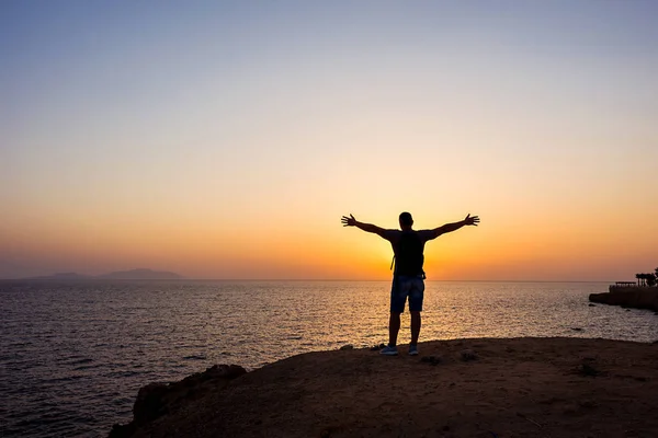 Gündoğumu arka plan üzerinde sahilde sırt çantası ile gezgin adam