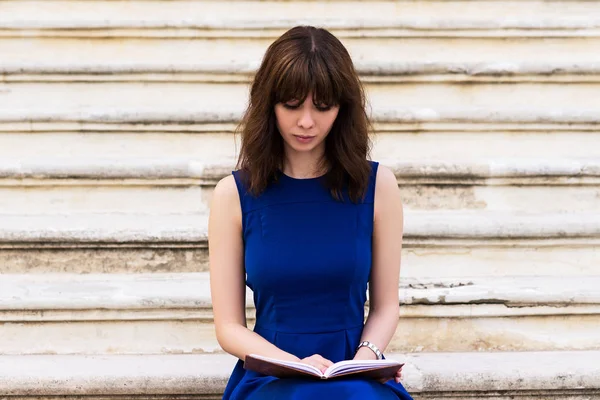Mavi elbise adımda oturan kız ve bir kitap okuma - Stok İmaj