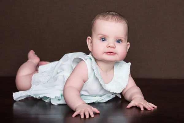 Souriant Petite Fille En Robe D Ete Avec De Grands Yeux Bleus Se Trouve Sur Son Ventre Sur Fond Brun Doux Adorable Stock Photo