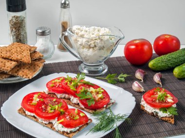 Karabuğday gevrek ekmek Yeşiller ve baharat bir tablo üzerinde beyaz forforor tabakta domates üzerine lor peynirli bulaşmış