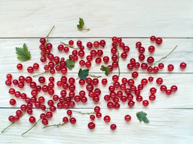 Çilek yeşil yaprakları ile birlikte ahşap arka plan üzerinde dağılmış büyük kırmızı kuş üzümü yukarıda close-up kaldırılır