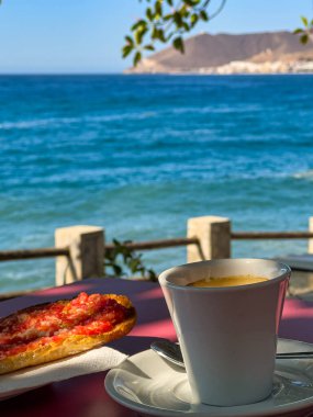 Espresso 'nun yakın çekimi, domates, yağ ve tuzlu tost Akdeniz ve arka planda bir kıyı köyü olan bir masada. Turizm ve sağlıklı yaşam tarzı kavramı.