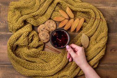 Kupa veya Kupası, sıcak Berry çay ile sarı sıcak örme eşarp sonbahar akçaağaç yaprakları ahşap arka plan üst görünüm düz yatıyordu sonbahar soğuk sezon kadın elini tutarak fincan çay