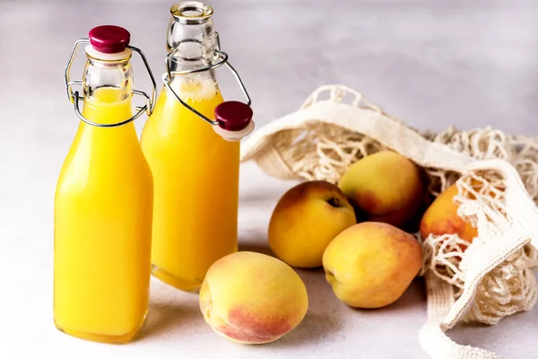 Natural Peach Juice in a Bottle and Eco Bag with Ripe Peaches Gray Background Healthy Diet Drink Horizontal