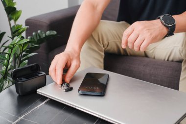 Modern dijital işitme cihazları, akıllı telefon ve şarj çantası şık bir ofis masasında, iş için hazırlanmış cihazlar. İş ortamı, ulaşılabilirlik ve profesyonel yaşam tarzı. Adam kulaklık kullanıyor. 