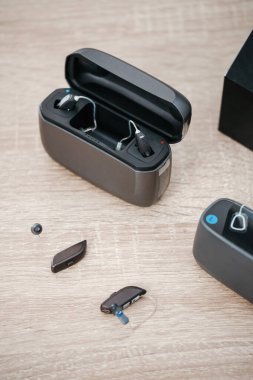 Modern dijital işitme cihazları, işitme cihazlarını odiyoloji kliniğindeki ahşap masada şarj ediyor. İşitme cihazı, şarj aleti ve tanıtım için kulak modeli..