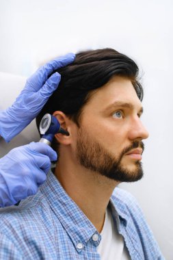 KBB doktoru, erkek hastayı otoskopla modern klinikte muayene ediyor. Kulak muayenesi sırasında eldiven ve far uzmanı. Yakın çekim.