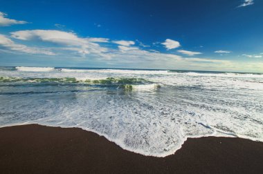 Halaktyr plaj. Kamçatka. Rusya Federasyonu. Karanlık neredeyse siyah renkli kum beach Pasifik Okyanusu. Taş dağları ve sarı çim bir arka plan üzerinde vardır. Hafif mavi gökyüzü.