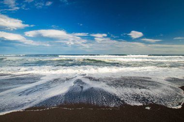 Halaktyr plaj. Kamçatka. Rusya Federasyonu. Karanlık neredeyse siyah renkli kum beach Pasifik Okyanusu. Taş dağları ve sarı çim bir arka plan üzerinde vardır. Hafif mavi gökyüzü.