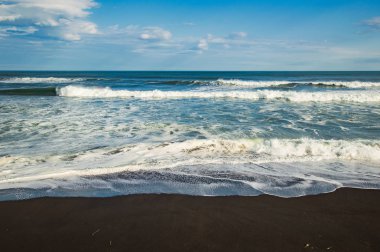 Halaktyr plaj. Kamçatka. Rusya Federasyonu. Karanlık neredeyse siyah renkli kum beach Pasifik Okyanusu. Taş dağları ve sarı çim bir arka plan üzerinde vardır. Hafif mavi gökyüzü