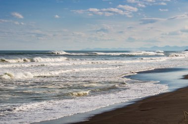 Halaktyr plaj. Kamçatka. Rusya Federasyonu. Karanlık neredeyse siyah renkli kum beach Pasifik Okyanusu. Taş dağları ve sarı çim bir arka plan üzerinde vardır. Hafif mavi gökyüzü