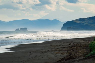 Halaktyr plaj. Kamçatka. Rusya Federasyonu. Karanlık neredeyse siyah renkli kum beach Pasifik Okyanusu. Taş dağları ve sarı çim bir arka plan üzerinde vardır. Hafif mavi gökyüzü