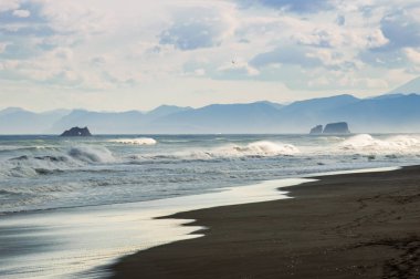 Halaktyr plaj. Kamçatka. Rusya Federasyonu. Karanlık neredeyse siyah renkli kum beach Pasifik Okyanusu. Taş dağları ve sarı çim bir arka plan üzerinde vardır. Hafif mavi gökyüzü