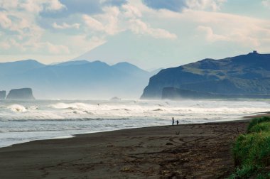 Halaktyr plaj. Kamçatka. Rusya Federasyonu. Karanlık neredeyse siyah renkli kum beach Pasifik Okyanusu. Taş dağları ve sarı çim bir arka plan üzerinde vardır. Hafif mavi gökyüzü