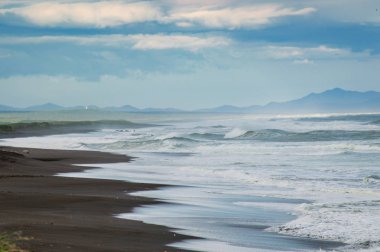 Halaktyr plaj. Kamçatka. Rusya Federasyonu. Karanlık neredeyse siyah renkli kum beach Pasifik Okyanusu. Taş dağları ve sarı çim bir arka plan üzerinde vardır. Hafif mavi gökyüzü