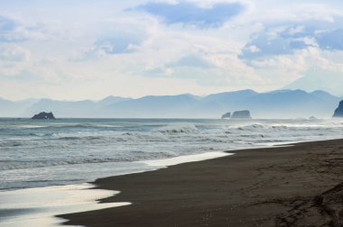Halaktyr plaj. Kamçatka. Rusya Federasyonu. Karanlık neredeyse siyah renkli kum beach Pasifik Okyanusu. Taş dağları ve sarı çim bir arka plan üzerinde vardır. Hafif mavi gökyüzü