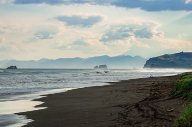 Halaktyr plaj. Kamçatka. Rusya Federasyonu. Karanlık neredeyse siyah renkli kum beach Pasifik Okyanusu. Taş dağları ve sarı çim bir arka plan üzerinde vardır. Hafif mavi gökyüzü