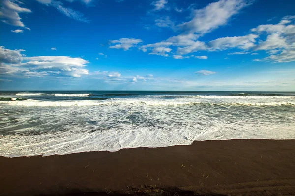 Halaktyr 비치입니다. 캄차카 반도입니다. 러시아 연맹입니다. 어두운 거의 블랙 색상 태평양 해변 모래. 돌 산과 노란 잔디 배경에 있습니다. 밝은 푸른 하늘 — 스톡 사진
