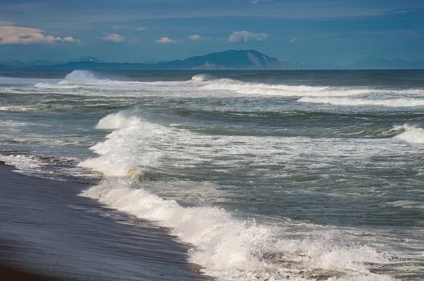Praia Halaktyr. Kamchatka. Federação Russa. Praia de areia de cor quase negra escura do Oceano Pacífico. Montanhas de pedra e grama amarela estão em um fundo. Céu azul claro — Fotografia de Stock