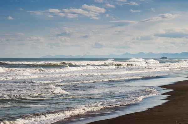Halaktyr beach. Kamchatka. Russian federation. Dark almost black color sand beach of Pacific ocean. Stone mountains and yellow grass are on a background. Light blue sky — Stock Photo, Image
