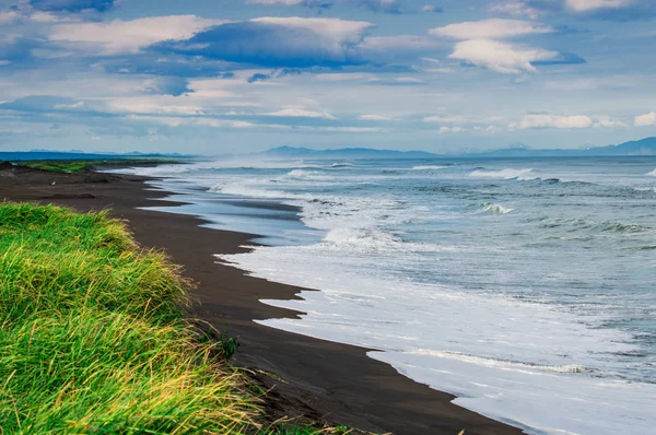 Halaktyr-Strand. kamchatka. Russische Föderation. dunkle fast schwarze Farbe Sandstrand des Pazifischen Ozeans. Steinberge und gelbes Gras sind auf einem Hintergrund zu sehen. hellblauer Himmel — Stockfoto