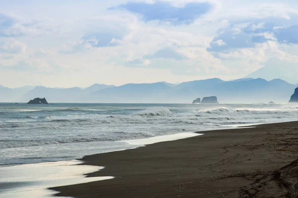 Halaktyr plaj. Kamçatka. Rusya Federasyonu. Karanlık neredeyse siyah renkli kum beach Pasifik Okyanusu. Taş dağları ve sarı çim bir arka plan üzerinde vardır. Hafif mavi gökyüzü
