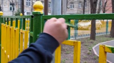 İşçi sarı ve yeşil çubuklar yapılan bir metal çit bir yeşil boya fırça ile boya