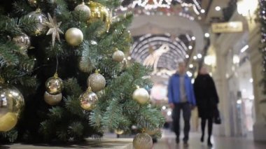Farklı altın toplarla süslenmiş Noel ağacı. İnsanlar odak noktasından içeri giriyor.