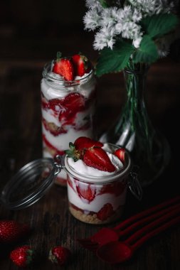 Katmanlı kremalı tatlı ve koyu ahşap arka plan üzerinde Karanfil Buketi iki kavanoz