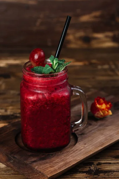 Koyu kırmızı dut güler yüzlü ve ahşap arka plan üzerinde siyah saman ile Mason kavanoza kupalar