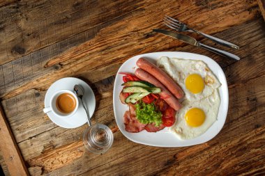 Kahve ve kızarmış yumurta pastırma, sosis ve sebze ahşap arka plan üzerinde beyaz tabakta servis kahvaltı. Üstten görünüm
