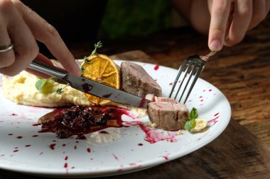 Adam tavşan eti plaka üzerinde yemeden önce kesiyor. Ahşap arka plan üzerinde