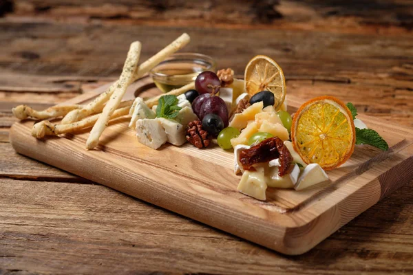 Cheese platter with assorted cheeses, grapes, olives, grissini and honey on the cutting bord wood background. Italian cheese and fruit platter