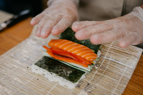 Usta bambu hasırından suşi yapıyor. Yuvarlanan suşi hazırlama sürecinin yakından görüntüsü.