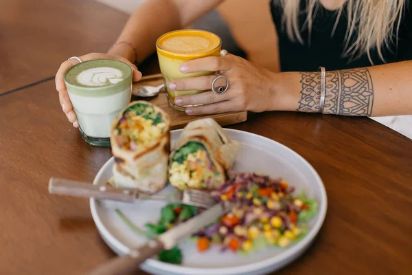 テーブルの上にサンドイッチとサラダを乗せたプレートの近くにコーヒーのグラスを置く女性 — ストック写真