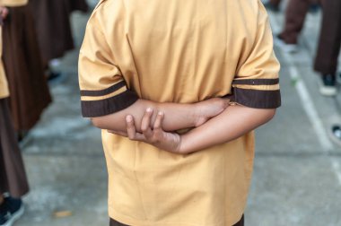 İzci üniforması giymiş bir öğrenci okul sırasının arkasında duruyor. Açık hava aktivitesi, disiplin ve odaklanma sırasında.