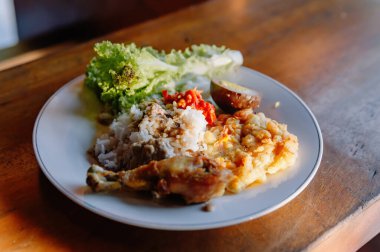 Ağız sulandırıcı bir tabak Nasi Campur, geleneksel Endonezya karışık pirinç yemeği tavuk, yumurta ve sebzeli ahşap bir masada.