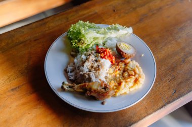 Ağız sulandırıcı bir tabak Nasi Campur, geleneksel Endonezya karışık pirinç yemeği tavuk, yumurta ve sebzeli ahşap bir masada.