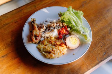 Ağız sulandırıcı bir tabak Nasi Campur, geleneksel Endonezya karışık pirinç yemeği tavuk, yumurta ve sebzeli ahşap bir masada.