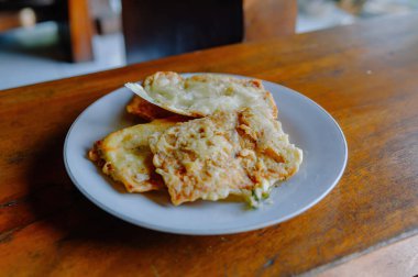 Kıtır kıtır ve lezzetli Tempe Mendoan, geleneksel Endonezya kızarmış tempeh, kırsal ahşap bir masada beyaz bir tabakta servis edilir.