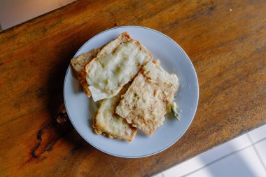 Kıtır kıtır ve lezzetli Tempe Mendoan, geleneksel Endonezya kızarmış tempeh, kırsal ahşap bir masada beyaz bir tabakta servis edilir.