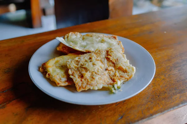Kıtır kıtır ve lezzetli Tempe Mendoan, geleneksel Endonezya kızarmış tempeh, kırsal ahşap bir masada beyaz bir tabakta servis edilir.